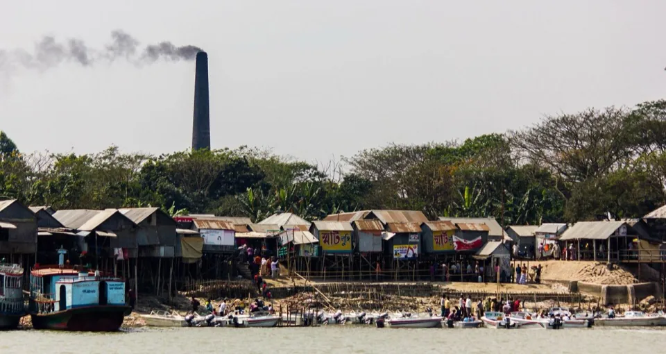 Riverside houses on stilts and small boats along the bank of a river in Barguna