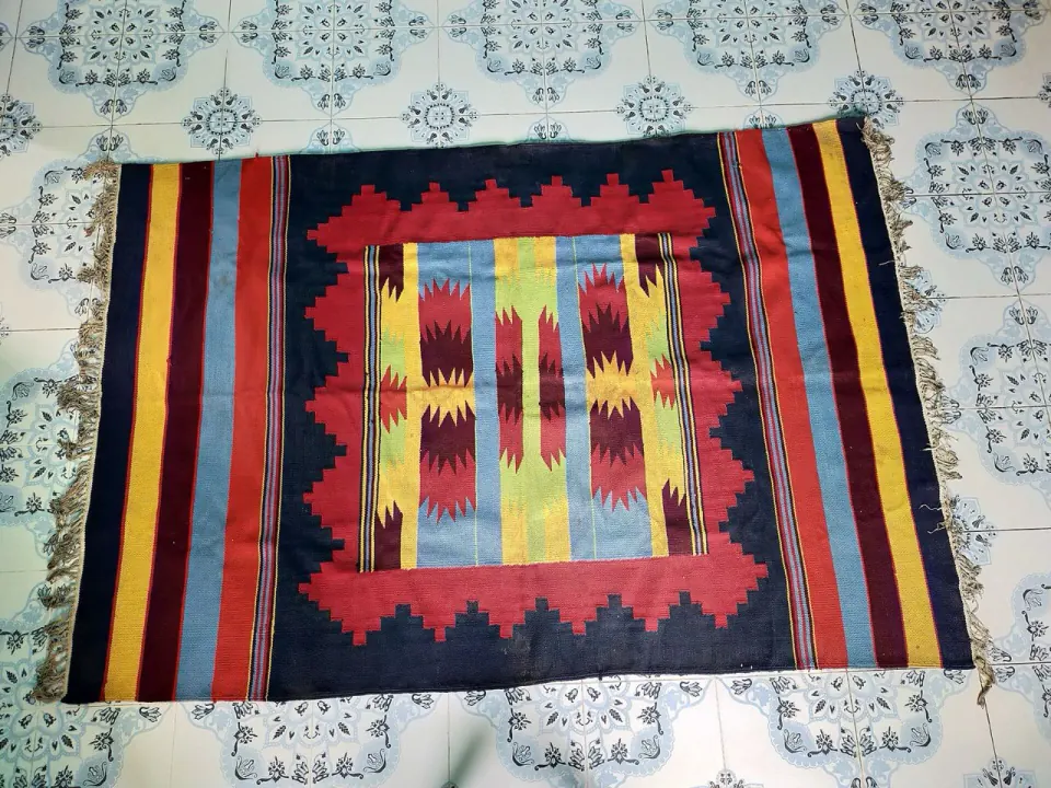 A colourful hand-woven shataranji rug with geometric patterns laid on a tiled floor